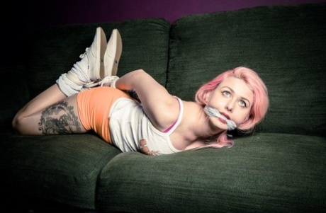 Caucasian girl with pink hair is left hogtied and cleave gagged on a sofa 97686631
